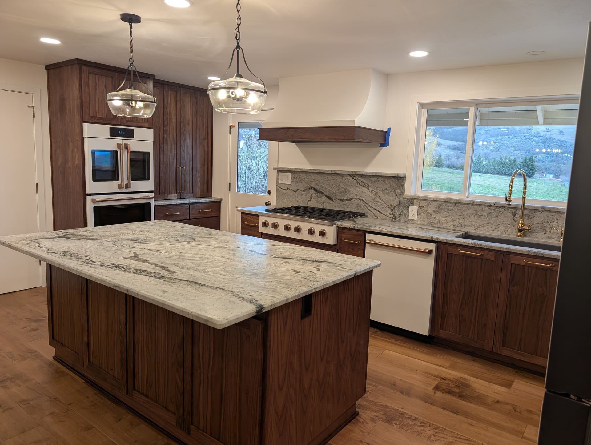 Custom walnut kitchen with waterfall granite island, brass fixtures, and mountain views